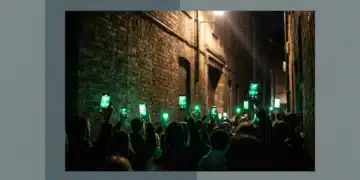 A low-angle professional photograph of a silhouetted crowd in a darkened urban alley, holding up smartphones emitting glowing green light, symbolizing digital activism and global discourse.