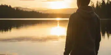 Sunrise over a lake with a person holding a phone, symbolizing digital detox and peace.